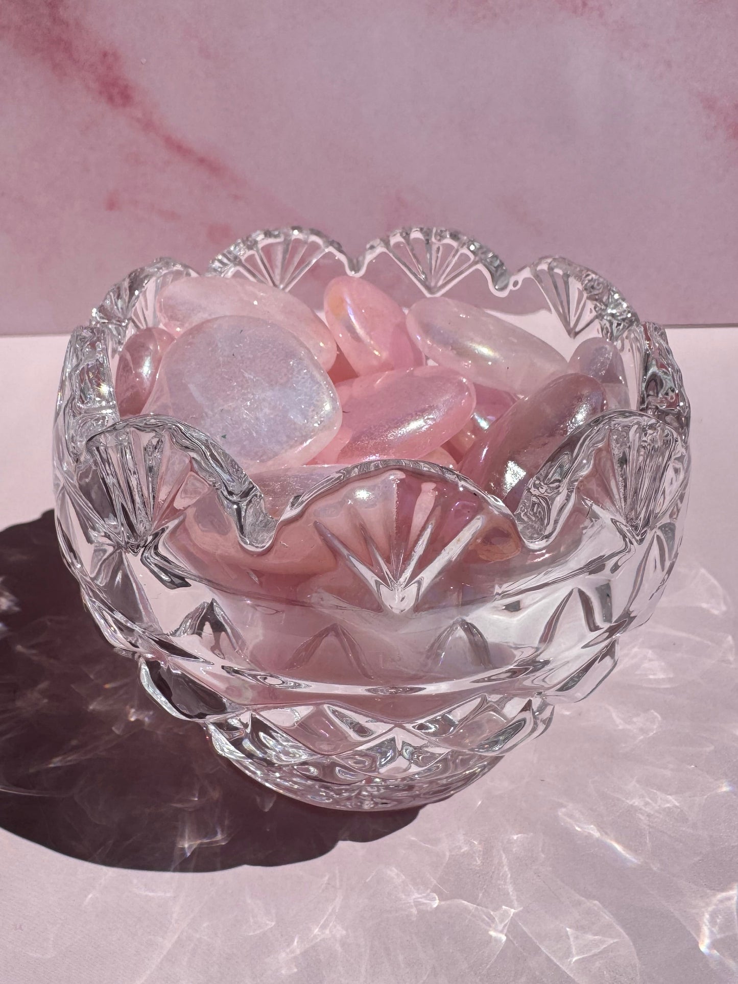 A Cut Crystal Mini Glass Bowl with scalloped edges is filled with smooth, translucent pink stones and rests on a light pink surface with soft shadows.