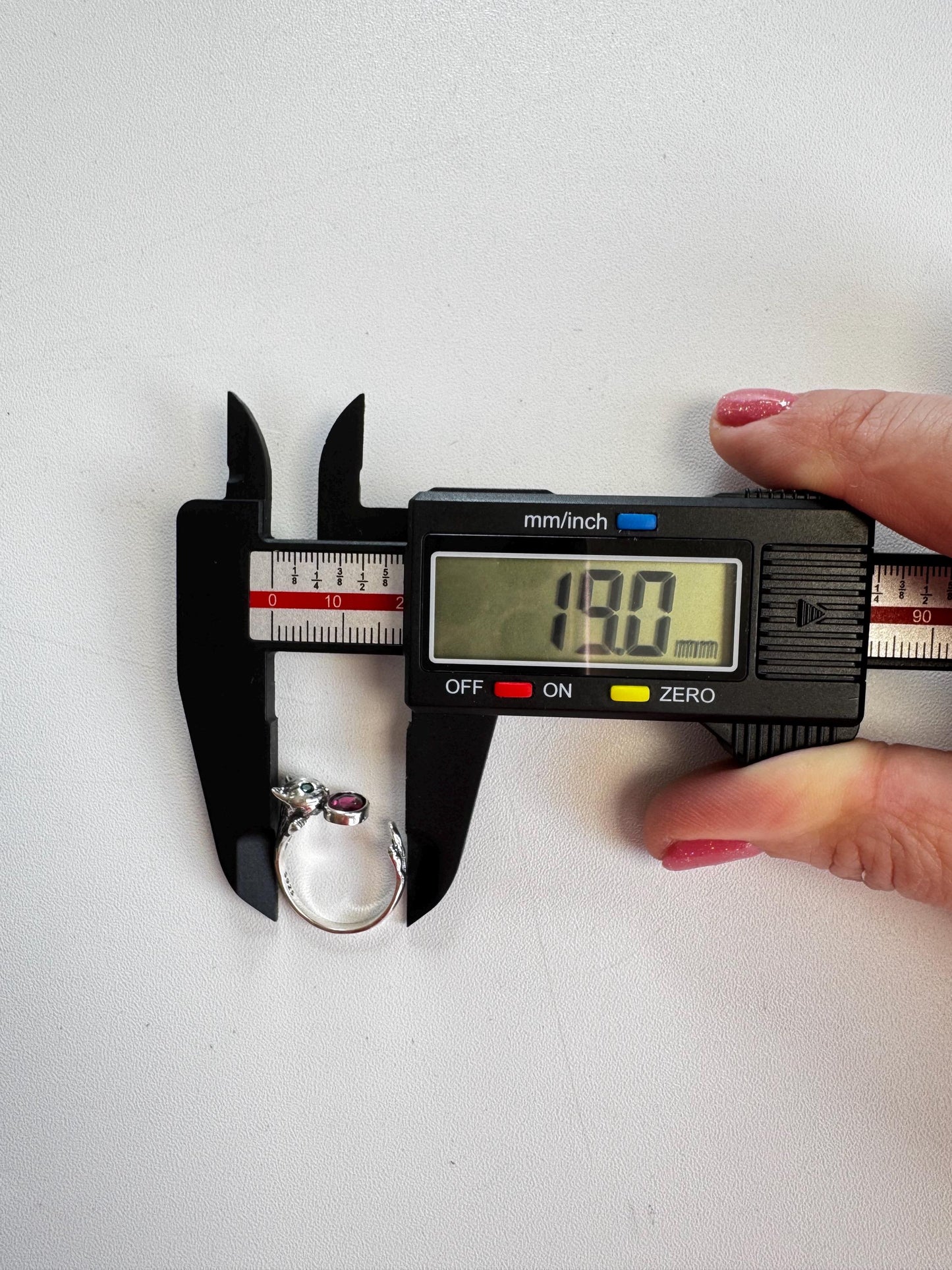 A digital caliper measures the diameter of a Sterling Silver Cat Ring with Pink Tourmaline Gemstone, Size 6.5 - Adjustable, showing 18.00 mm on the screen as a hand holds it against a white background.