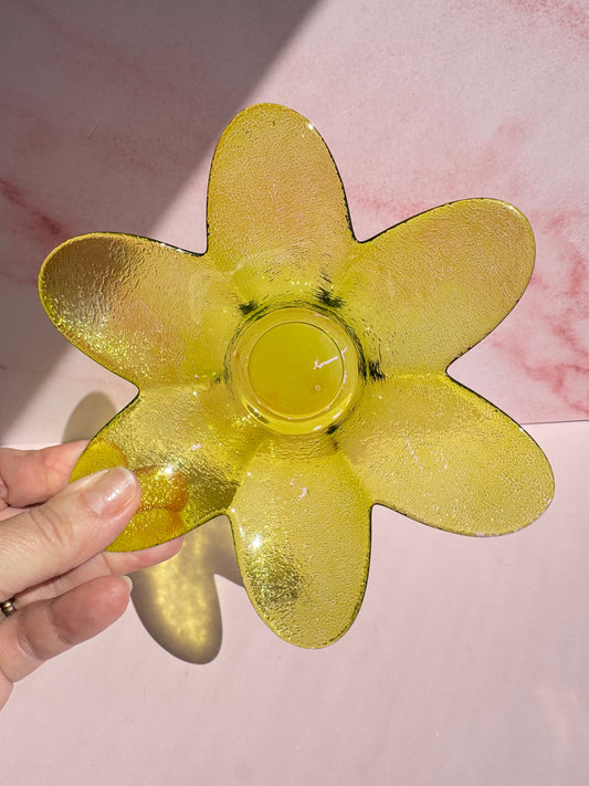 A hand holds the Green Flower Glass Bowl (Imperfect), a green, flower-shaped glass display bowl, against a pink background.