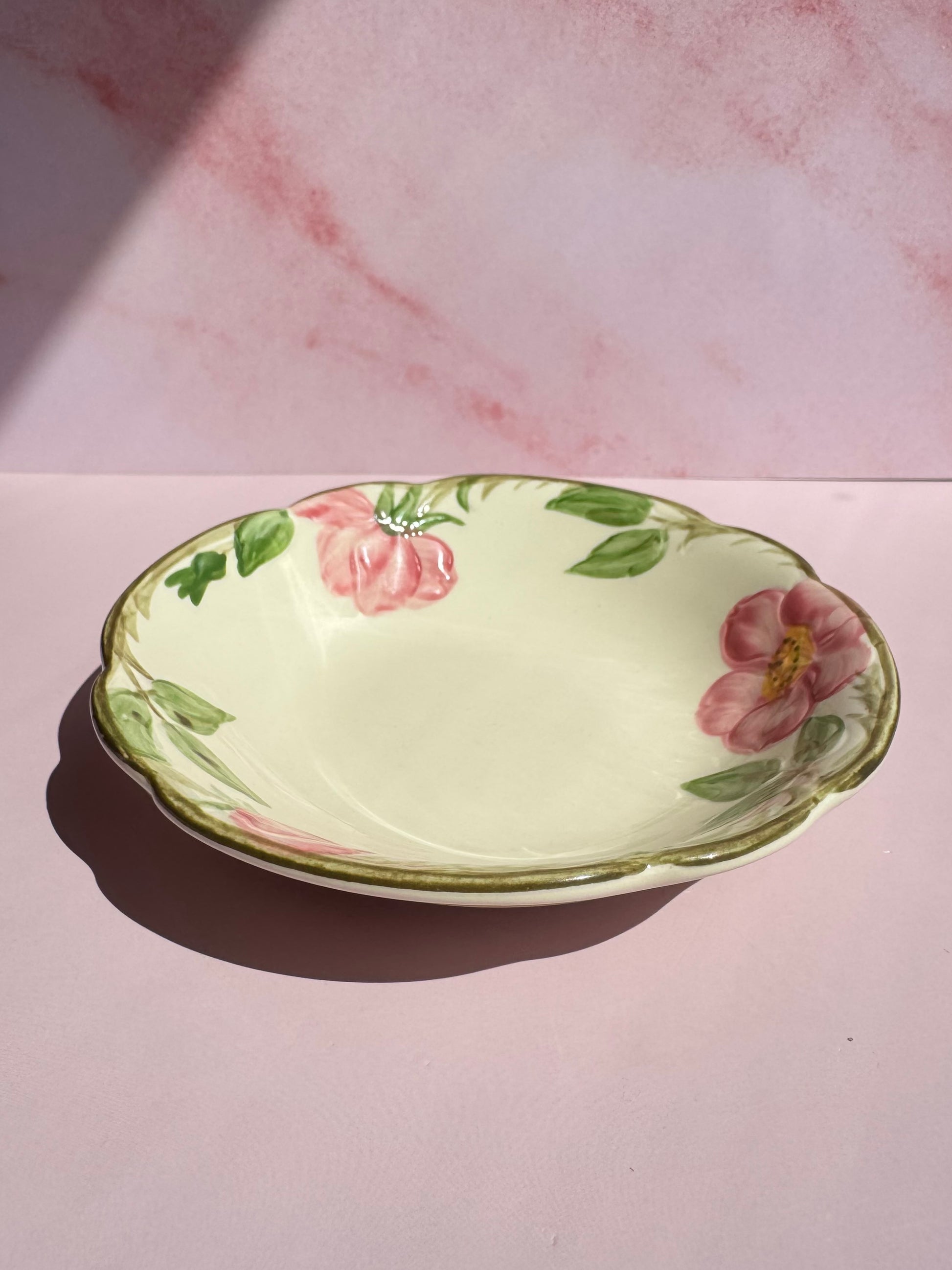 The Desert Rose Berry Bowl, featuring hand-painted pink flowers and green leaves in the classic Franciscan Earthenware style, sits on a pink surface with a pink and white background.