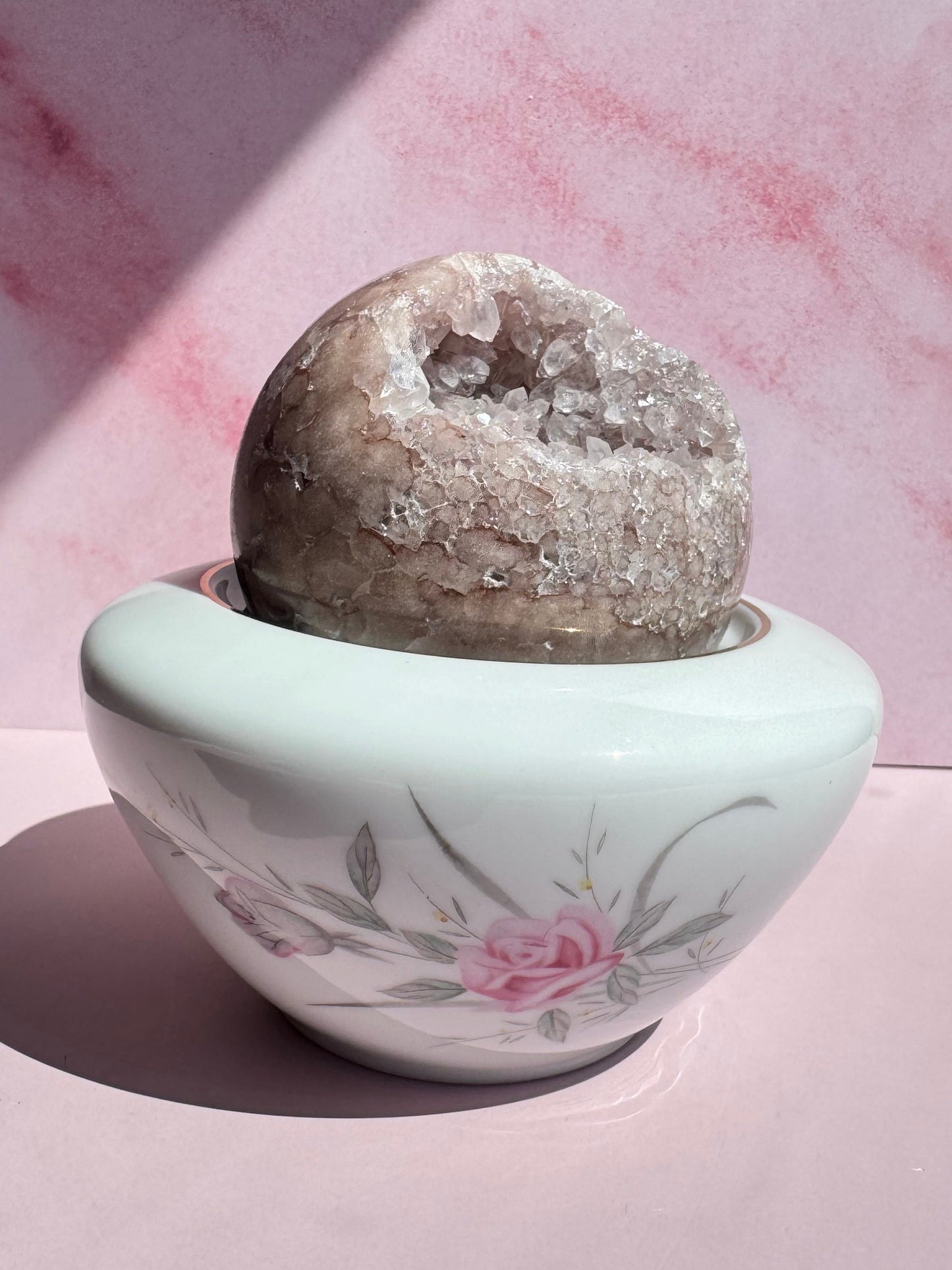 A geode is placed in a Porcelain Floral Sugar Bowl, set against a pink marbled background.