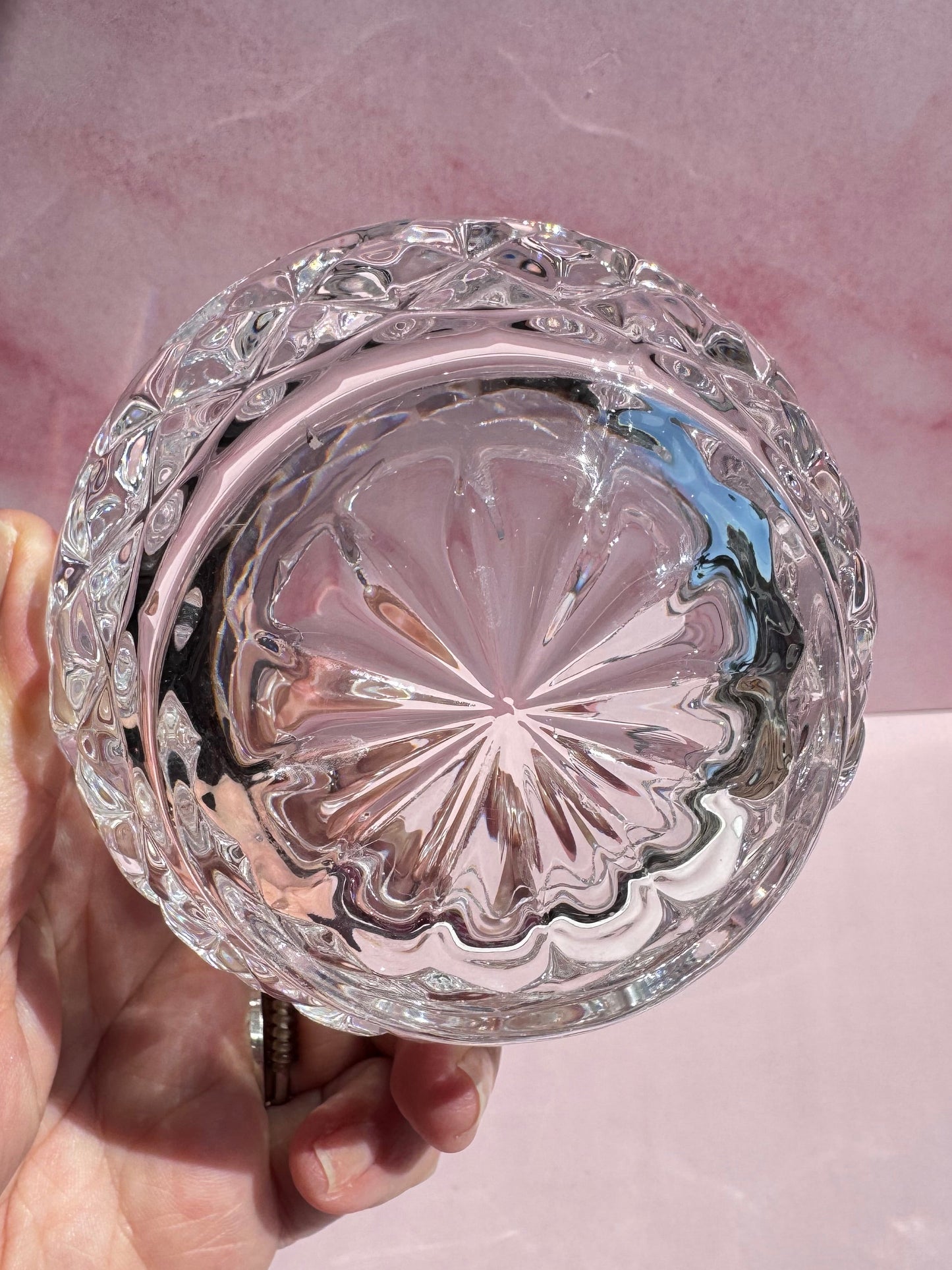 A hand holds the Cut Crystal Mini Glass Bowl, showcasing its clear, round design with a decorative faceted pattern and elegant scalloped edges, viewed from above against a pale pink background. The bowl’s edges catch the light beautifully.