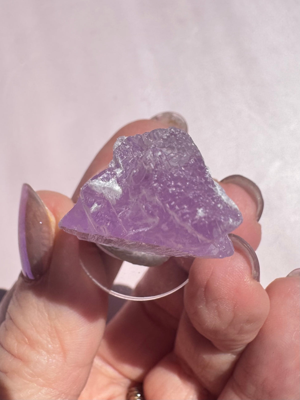 A hand holding a rough, translucent piece of Lavender Kunzite (Spodumene) - Item A against a light background, showcasing the natural beauty of this healing crystal.