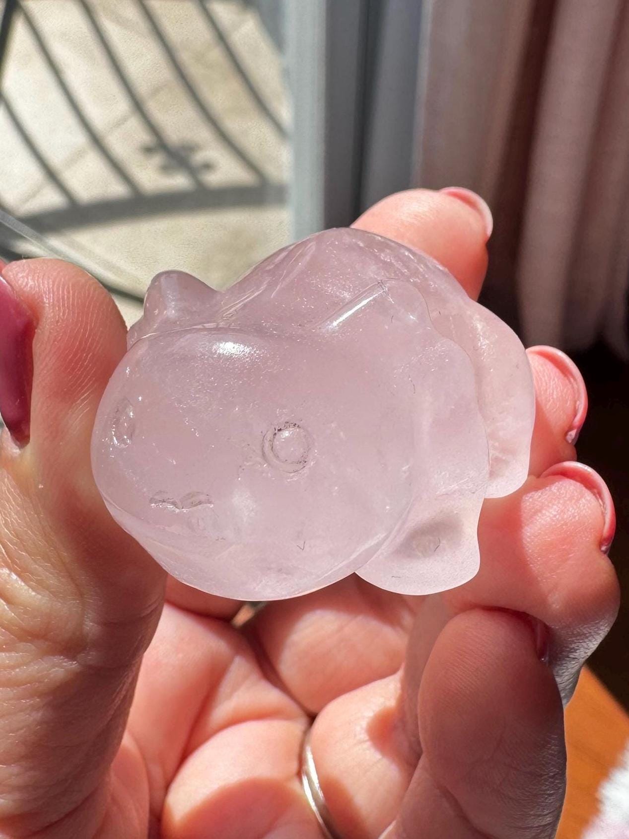 A hand holds a small Rose Quartz Axolotl 2" carving, displaying the pink crystal's beauty in natural sunlight—a perfect Rose Quartz crystal gift.