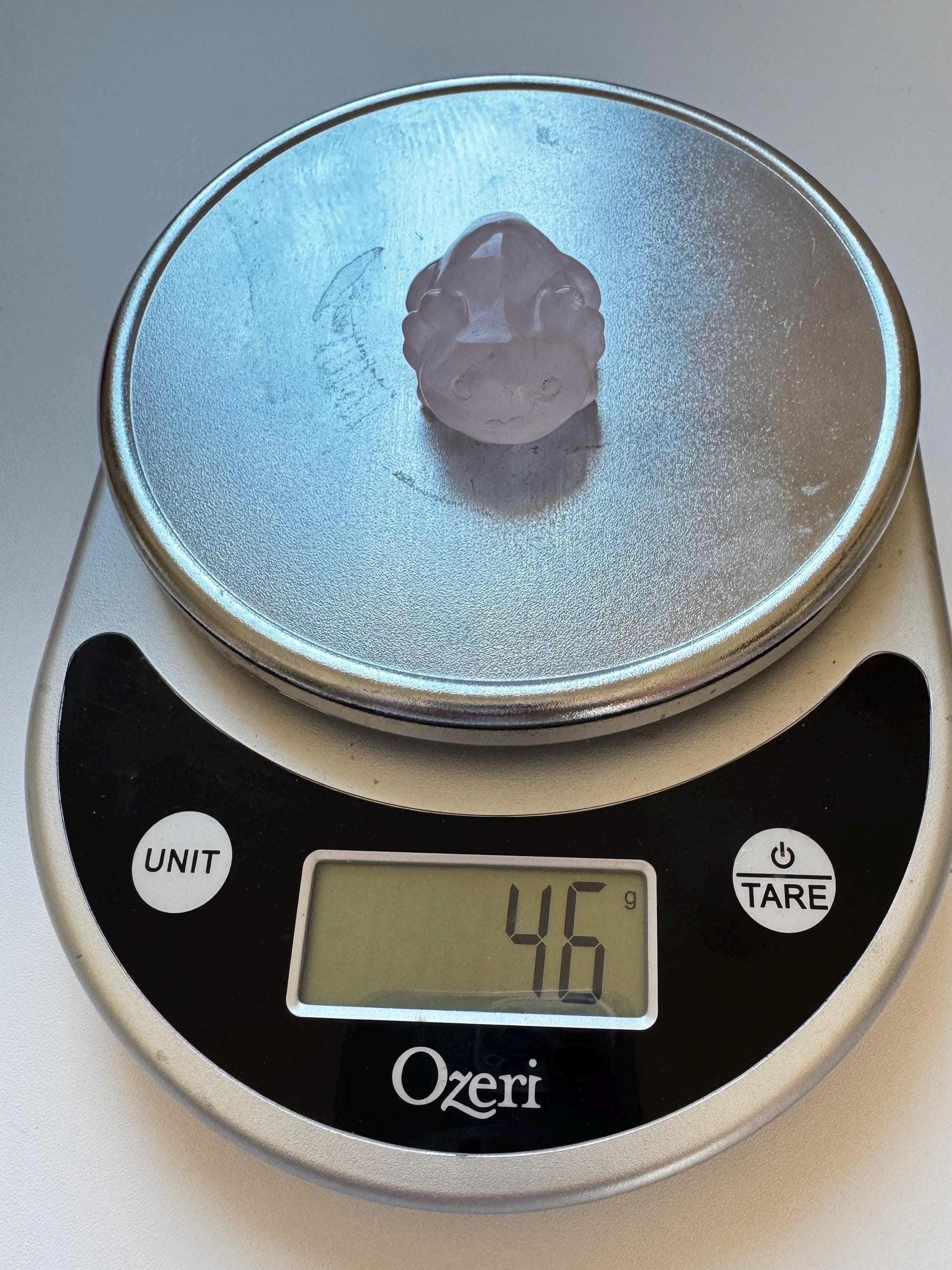 A Rose Quartz Axolotl 2" Carving sits on a digital kitchen scale, showing a weight of 4.6 grams.