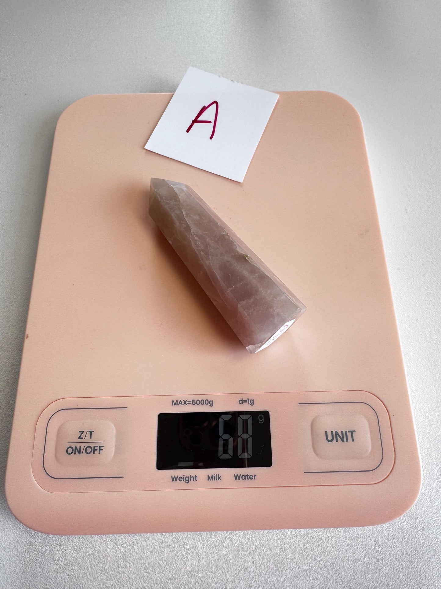 A pink digital kitchen scale shows 68 grams with a "Small A" Rose Quartz Tower (3"–3.6")—the stone of unconditional love—from the YOU CHOOSE collection, and a paper labeled "A" on top.