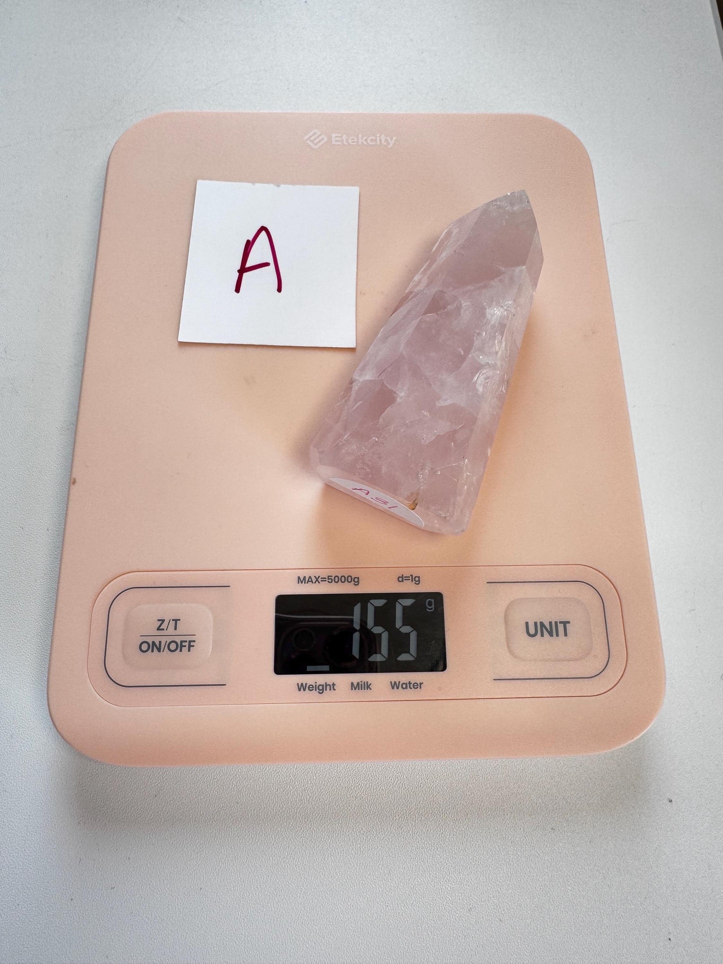 A pink digital kitchen scale shows 155 grams, with a Nice Quality Rose Quartz Obelisk Tower from Brazil (3.6"–3.8") and a paper marked “A” placed on it.
