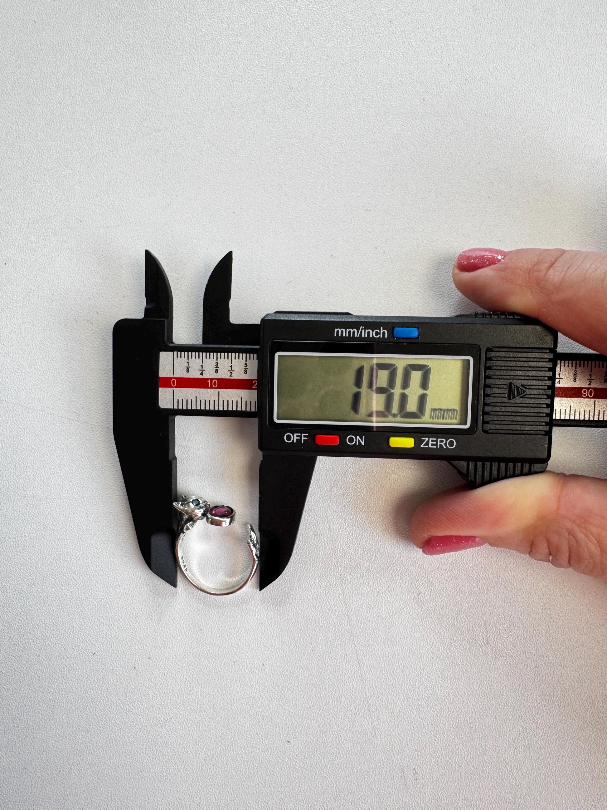 A digital caliper measures the diameter of a Sterling Silver Cat Ring with Pink Tourmaline Gemstone, Size 6.5 - Adjustable, showing 18.00 mm on the screen as a hand holds it against a white background.