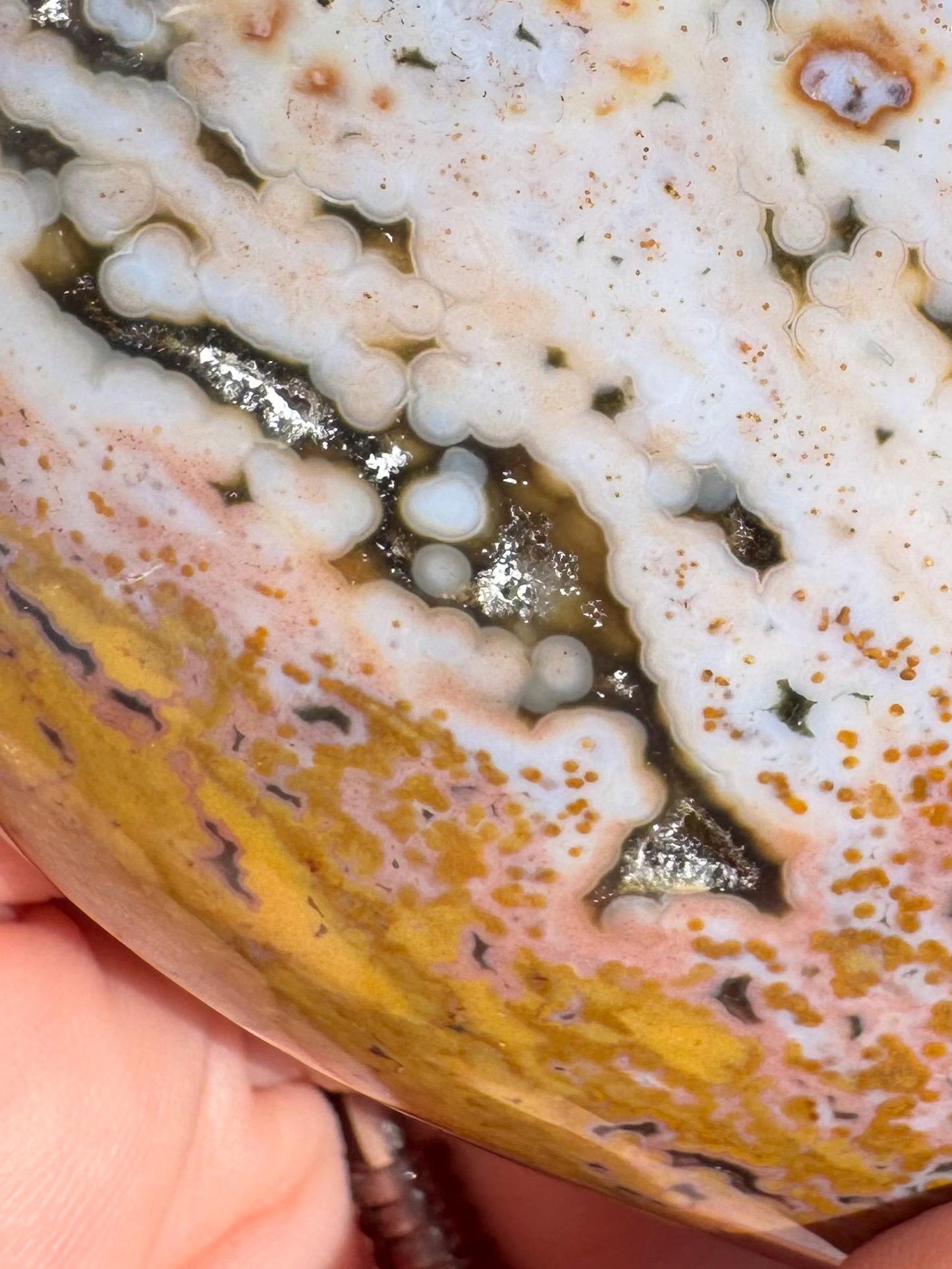 Close-up of a person holding the Ocean Jasper Heart from Madagascar - Item C, a polished healing stone featuring patterns of white, yellow, pink, and dark lines and spots.