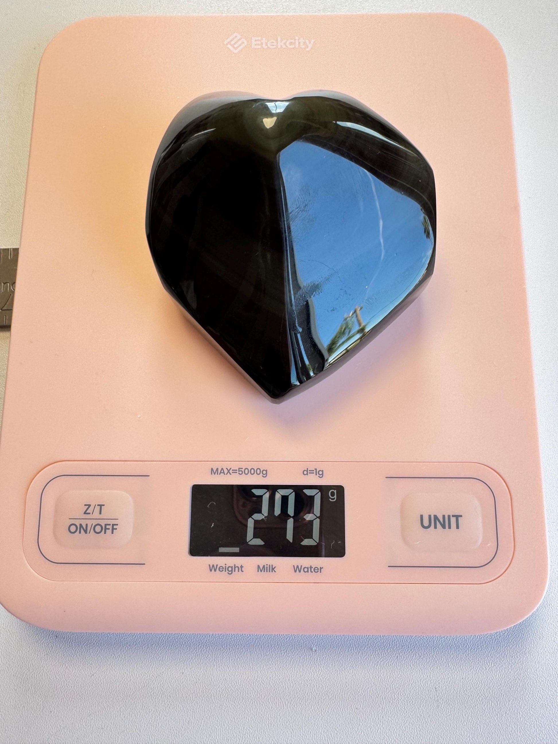 A Rainbow Obsidian Heart Carving from Mexico (ITEM G) sits on a pink digital kitchen scale, showing a weight of 291 grams.