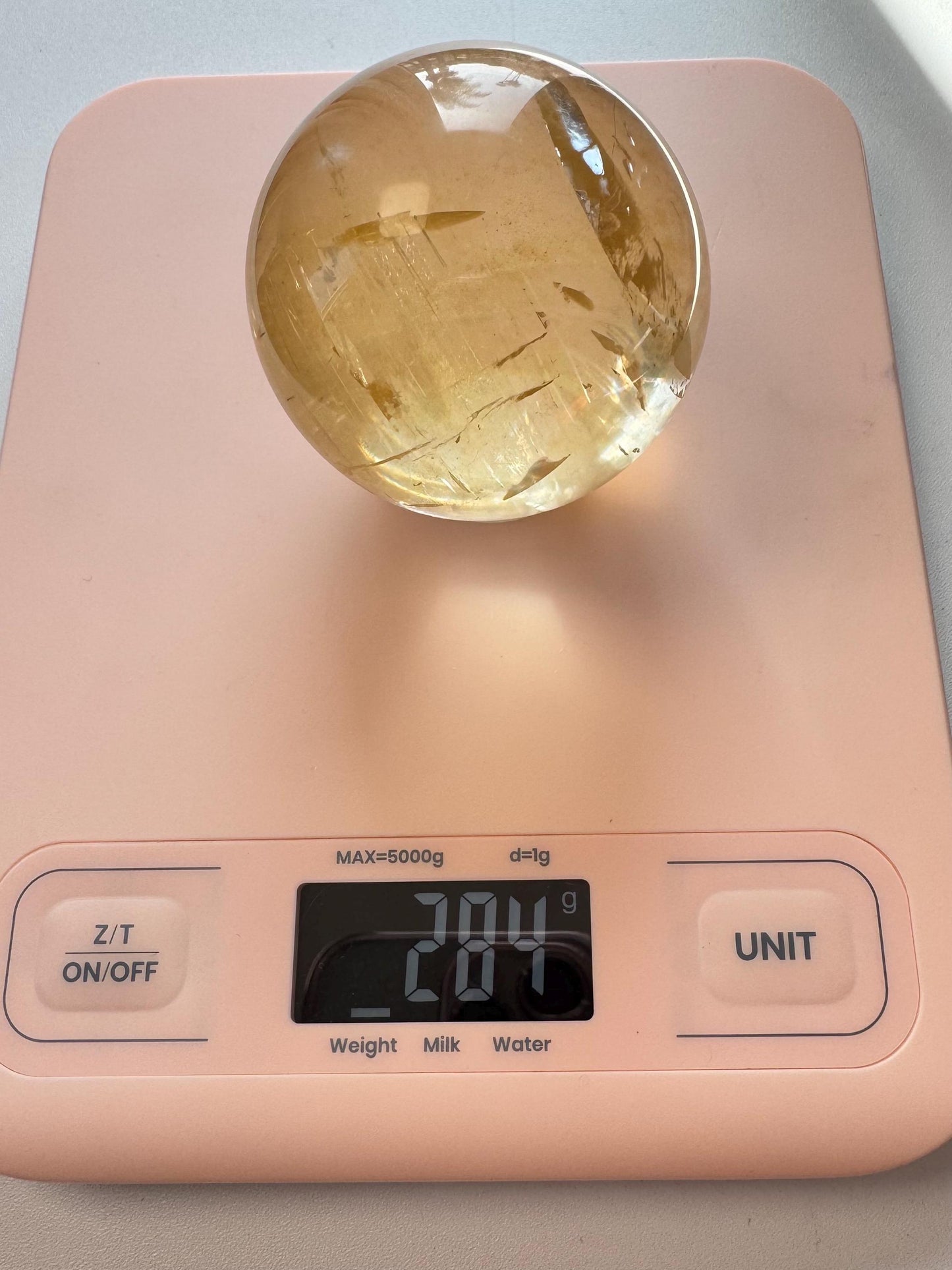 A Honey Calcite Sphere (58 mm diameter), known for boosting motivation, rests on a pink digital scale showing 284 grams.
