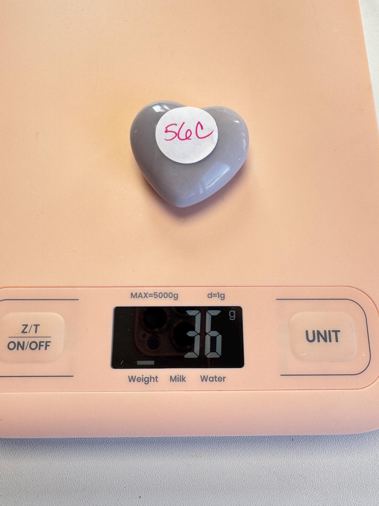 A Lavender Fluorite Heart Carving from Mexico (YOU CHOOSE), labeled "56C," rests on a digital scale showing 36 grams, highlighting the allure of expertly carved healing crystals.