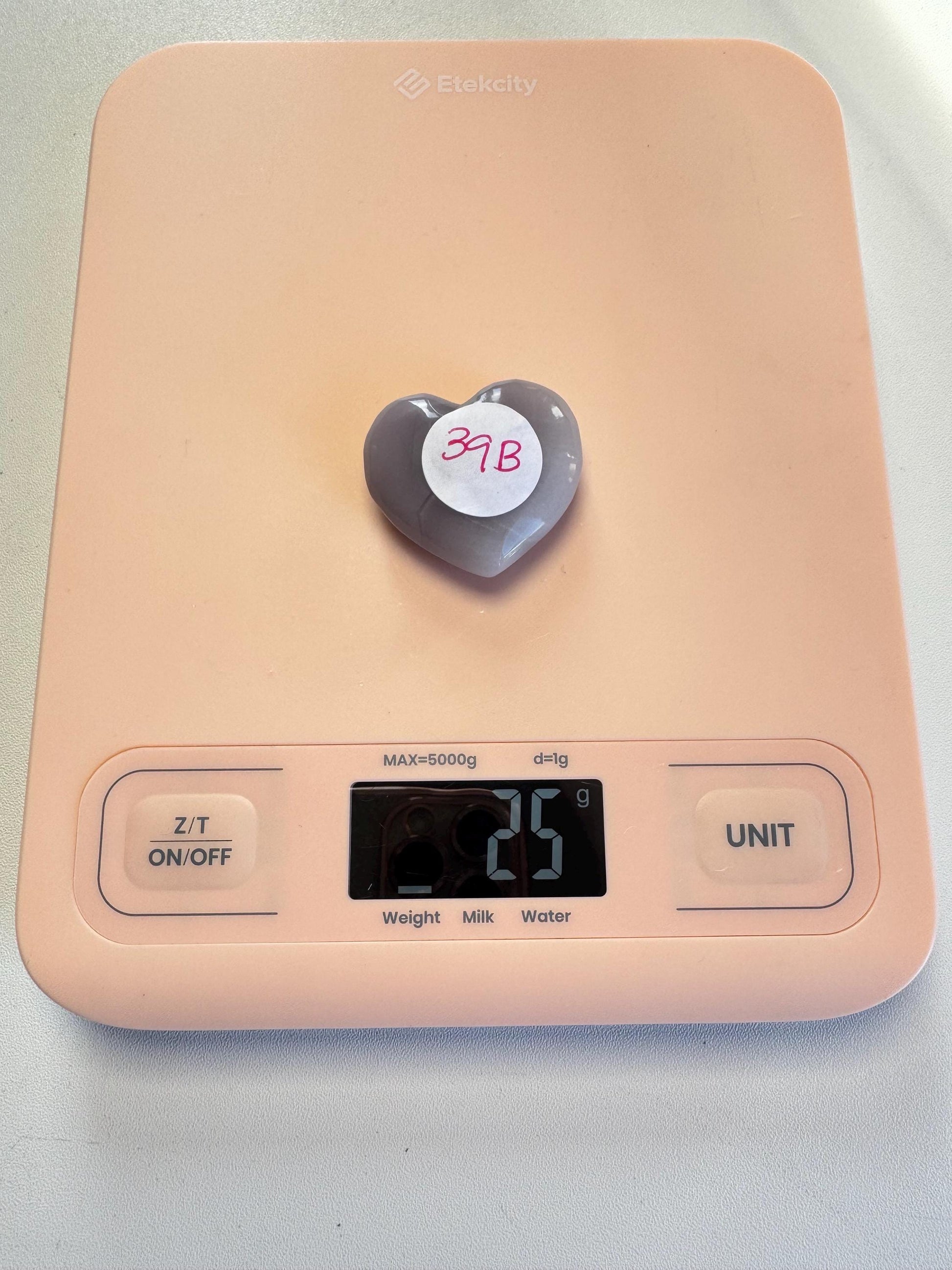 A Lavender Fluorite Heart Carving from Mexico (YOU CHOOSE), labeled "3B," rests on a pink digital kitchen scale showing 26 grams—ideal for healing crystal collectors.