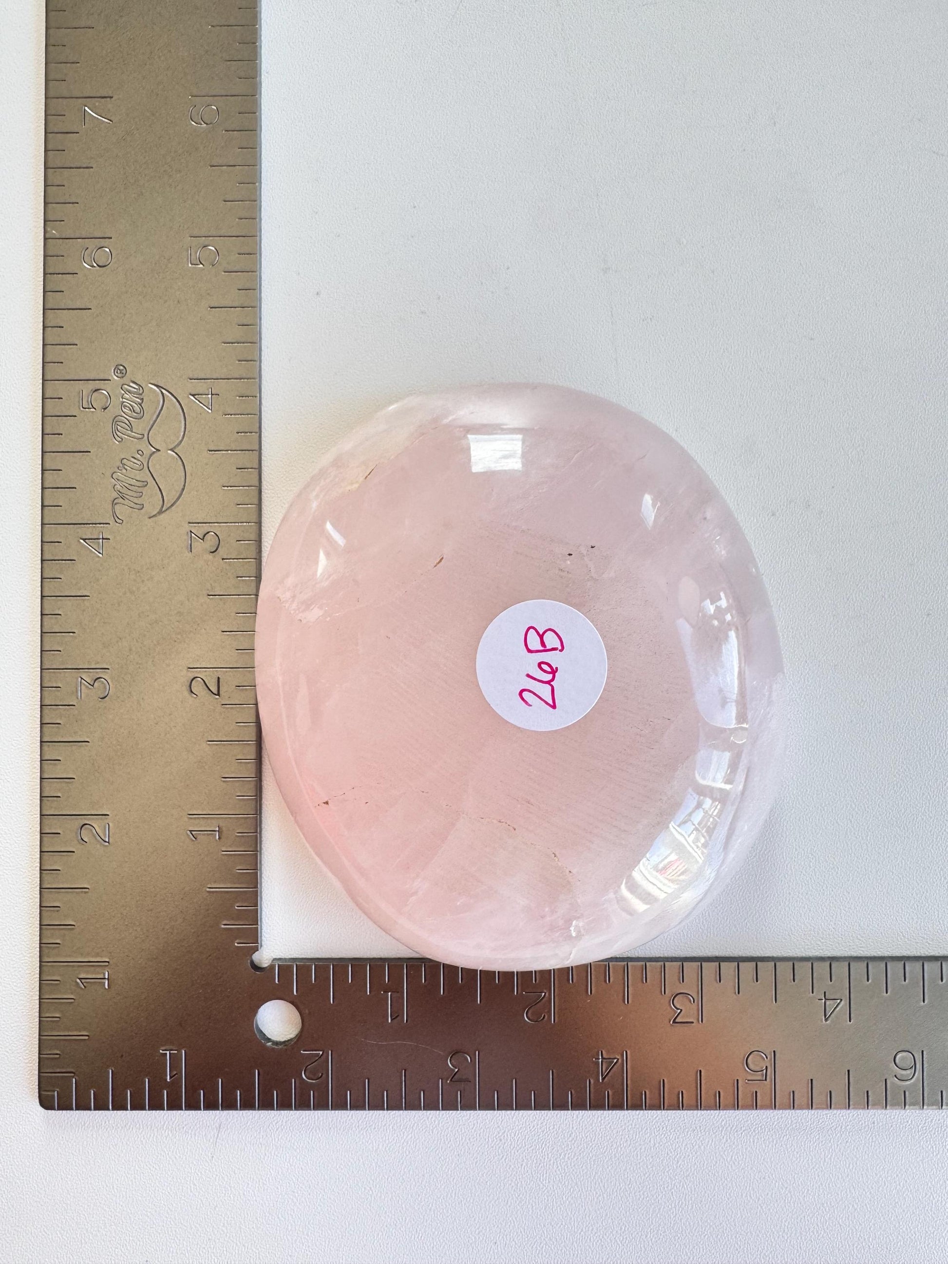 A Rose Quartz Bowl - ITEM B, pink crystal bowl, is placed beside two metal rulers showing it's about 3.5" long and 2.5" wide—perfect for holding small tumbles, jewelry, or trinkets and ideal for crystal collectors.