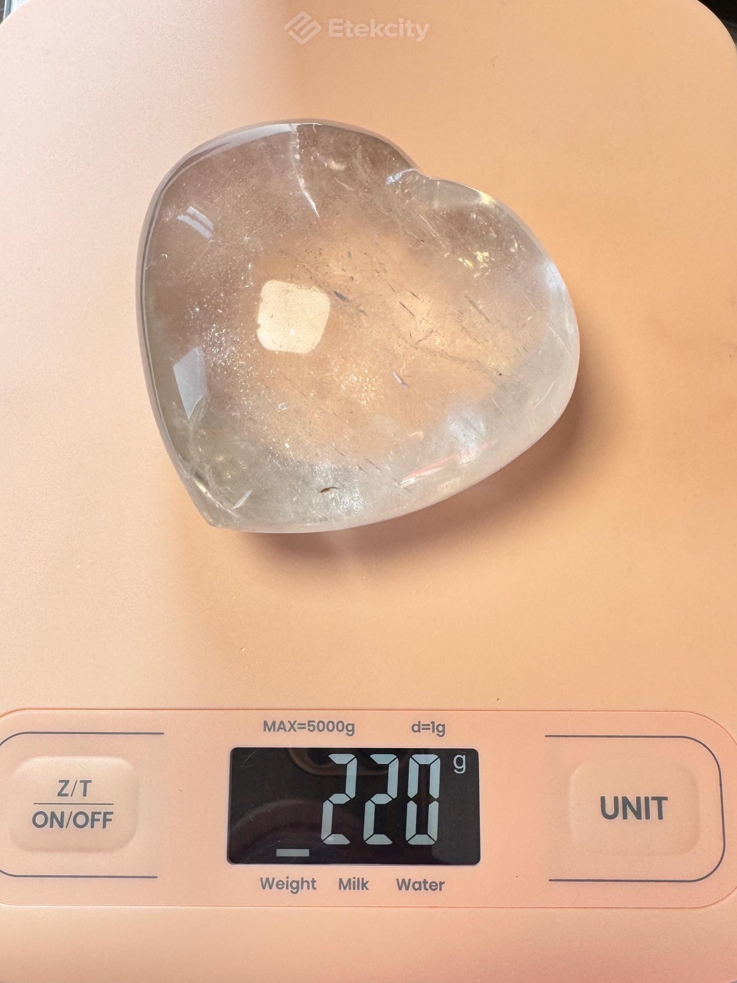 A Clear Quartz Heart Carving - Very High Clarity Crystal sits on a digital scale, weighing 220 grams—ideal for crystal healing or as an eye-catching quartz centerpiece.