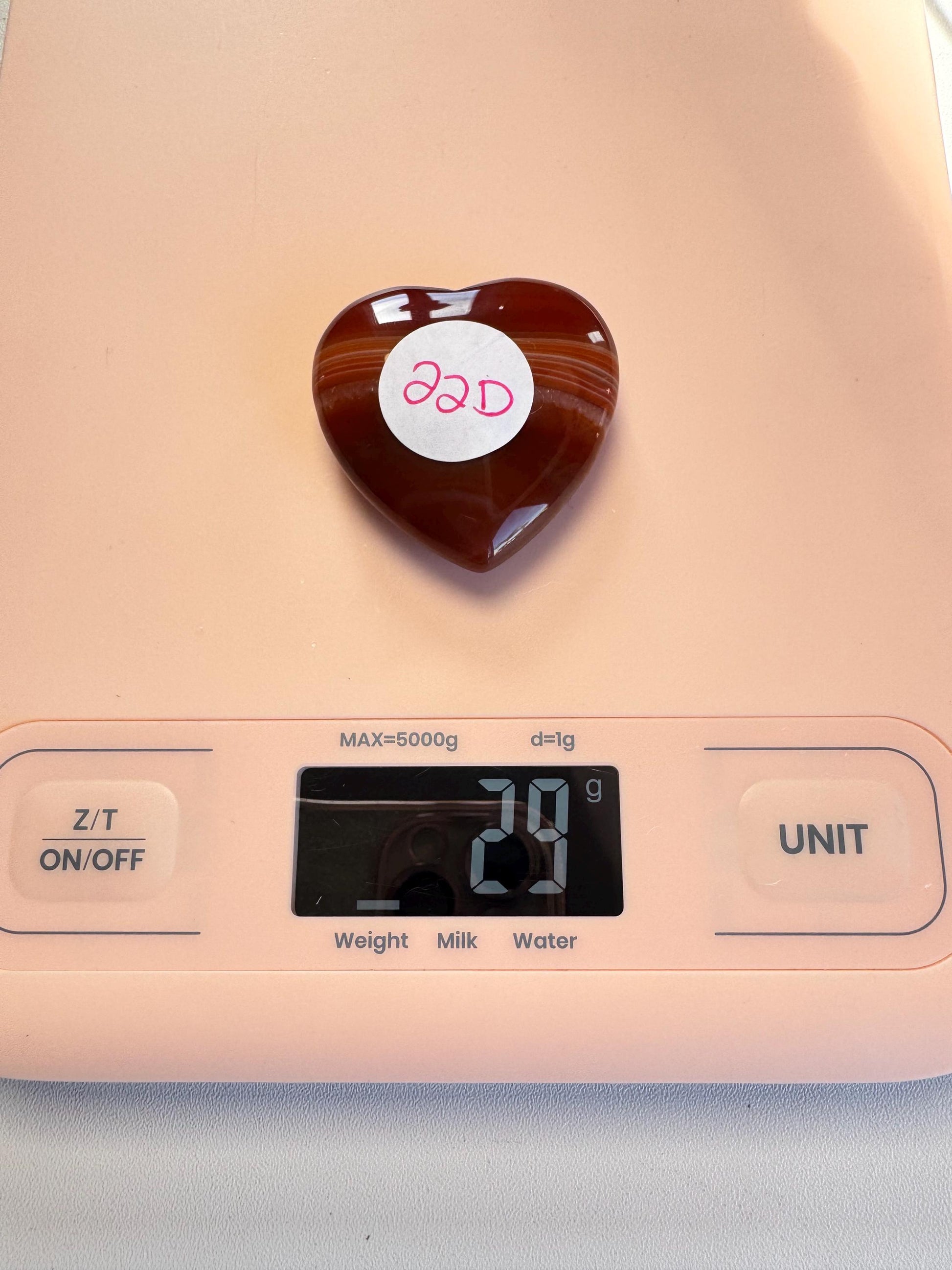 A Small Carnelian Heart Carving - YOU CHOOSE is shown on a digital scale reading 29 grams.