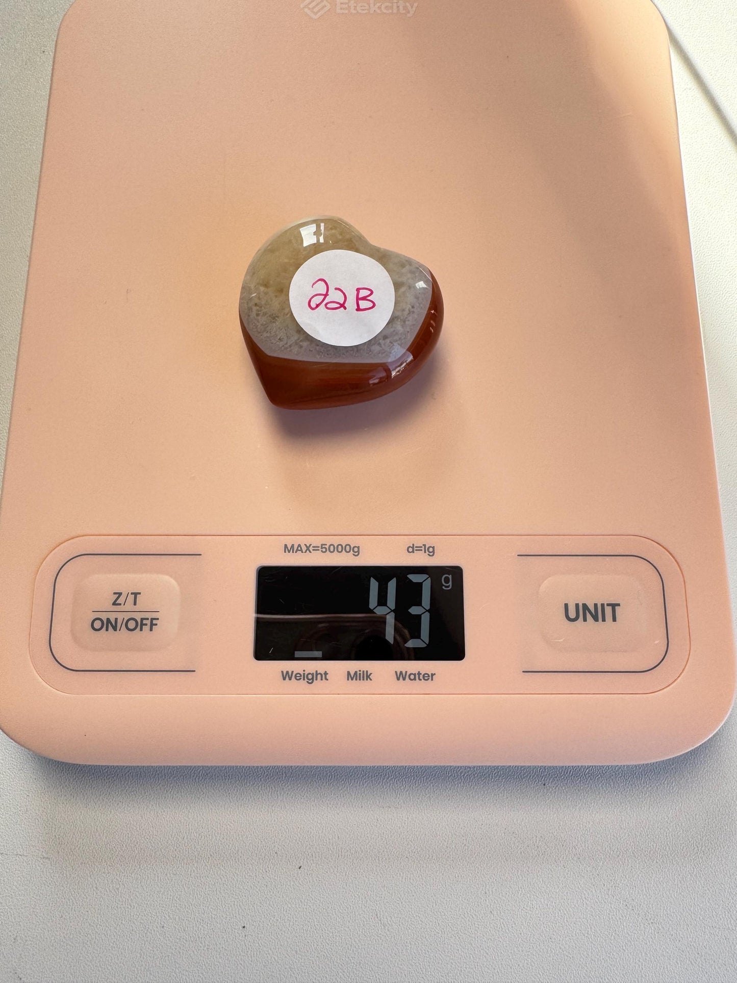 A Small Carnelian Heart Carving - YOU CHOOSE is shown on a digital kitchen scale reading 43 grams, highlighting this energizing crystal among a selection of unique healing stones.