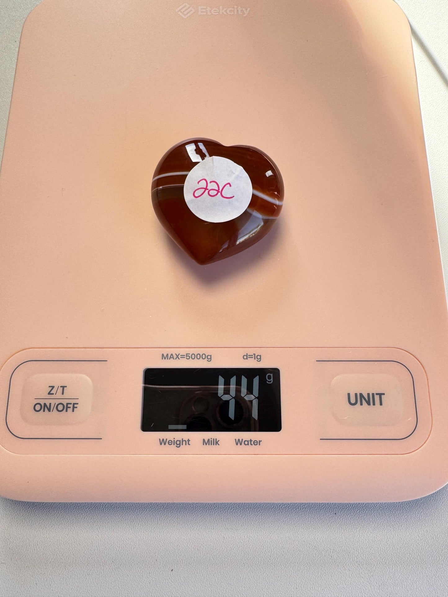 A Small Carnelian Heart Carving - YOU CHOOSE, labeled "22c," rests on a pink digital scale showing 44 grams, highlighting this beautiful and energizing healing crystal.