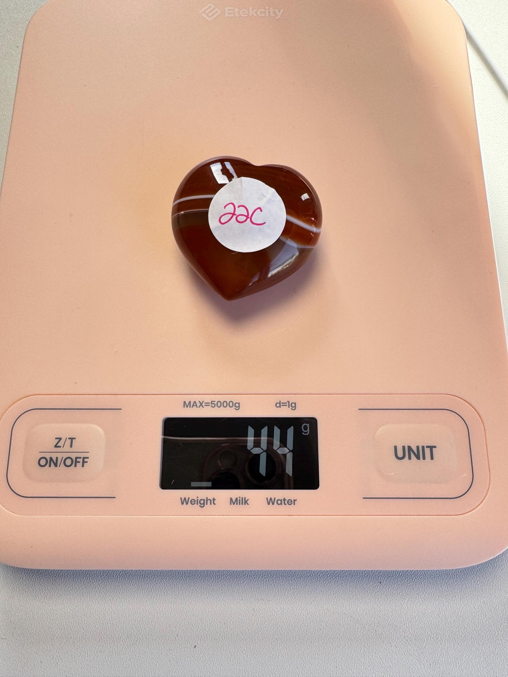 A Small Carnelian Heart Carving - YOU CHOOSE, labeled "22c," rests on a pink digital scale showing 44 grams, highlighting this beautiful and energizing healing crystal.